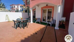Un pati amb taula i cadires, una porta corredissa de vidre, i un edifici amb balcons al fons.