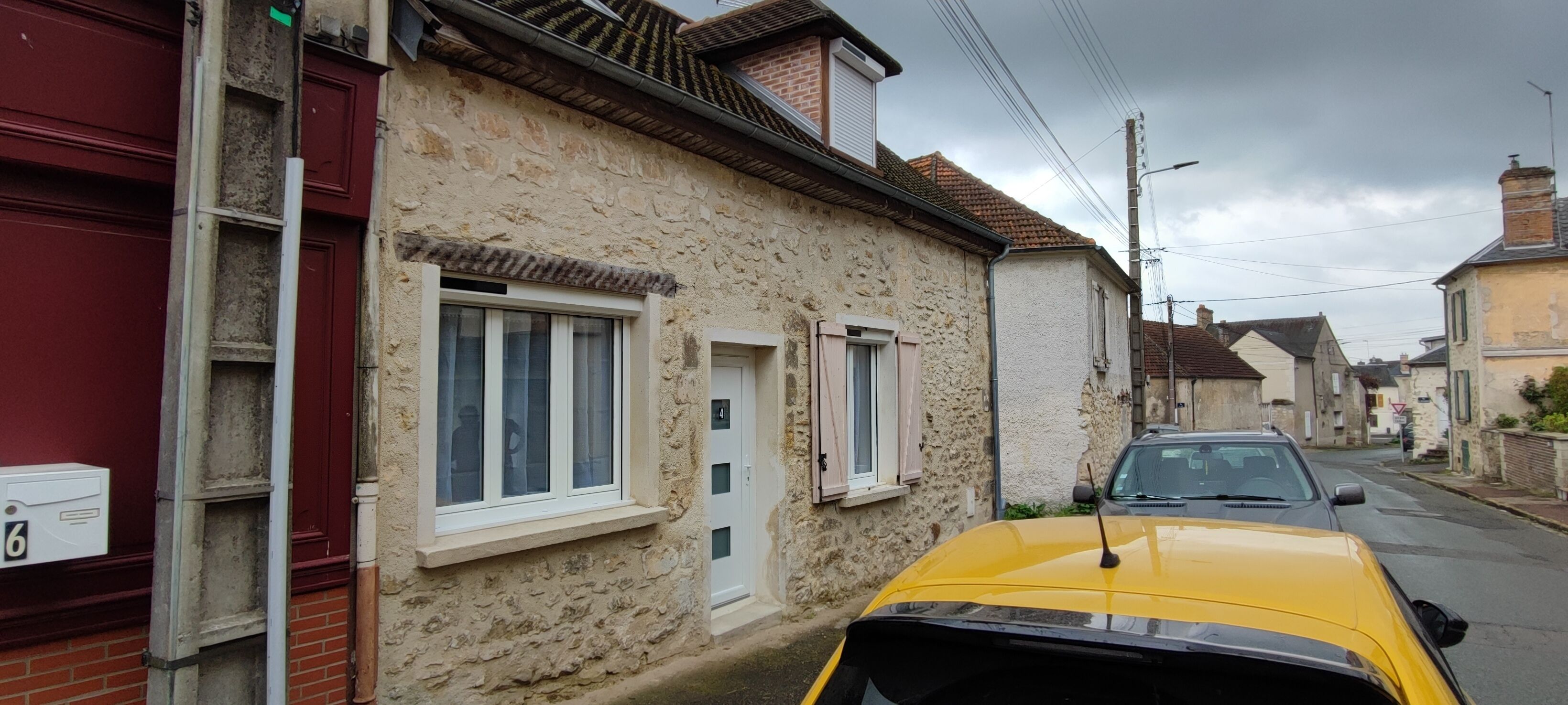 Une rue étroite bordée d’immeubles en pierre, une voiture jaune garée sur le côté et une boîte aux lettres sur la gauche.