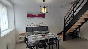 Spiseområde med bord, stole, dekorativ vægpynt, en trappe og et hvidt skab.