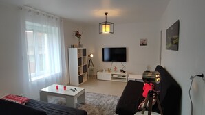 En stue med sofa, sofabord, fjernsyn, reol og lampe.