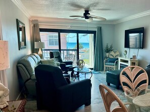 Ein Wohnzimmer mit einer Couch, Sesseln, einem Tisch, einem Deckenventilator und Blick auf den Ozean.
