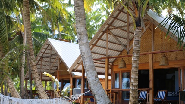 A resort with wooden cabins, palm trees, and a hammock. - Ombak Biru Resort (Sipura Island)