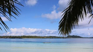 A beach with clear water, a boat, and a distant shoreline. - Ombak Biru Resort (Sipura Island)