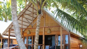 A wooden building with a thatched roof, large windows, and a porch area with chairs. - Ombak Biru Resort (Sipura Island)