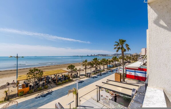 A beachside view with a restaurant, palm trees, and a clear sky. - Sea View Apartment Durr s Waterfront (Durrës)