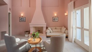 Ein Zimmer mit Kamin, zwei Sesseln, einem Sofa, einem Tisch mit Vase und zwei Wandlampen.