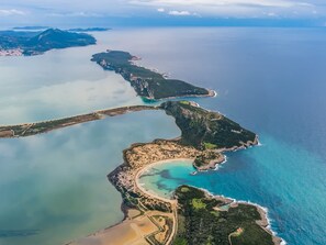 Oversigtsbillede af et kystområde med strand, klart vand og omkringliggende landskabsformer.