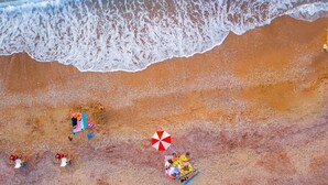 Luftaufnahme eines Strandes mit Wellen, einem Sandstrand und einigen Strandsonnenschirmen.