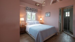 Ein Schlafzimmer mit einem Bett, zwei Nachttischlampen, einem Fenster mit Vorhang und einer Dusche.