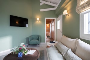 Ein Zimmer mit einer Couch, einem Sessel, einem Couchtisch mit einer Vase und einem an der Wand befestigten Flachbildfernseher.