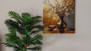 A potted plant, a painting, and a black ottoman against a wall. - Sun Sea Apartment Durr s Waterfront (Durrës)