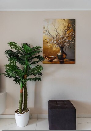 A potted plant, a painting, and a black ottoman against a wall. - Sun Sea Apartment Durr s Waterfront (Durrës)