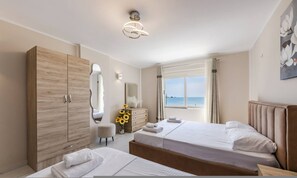 Een hotelkamer met twee bedden, een houten garderobe, een spiegel, een dressoir, een vaas met zonnebloemen en uitzicht op zee.