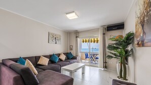 A living room with a sofa, a coffee table, a potted plant, and a view of the sea through a glass door. - Sun Sea Apartment Durr s Waterfront (Durrës)