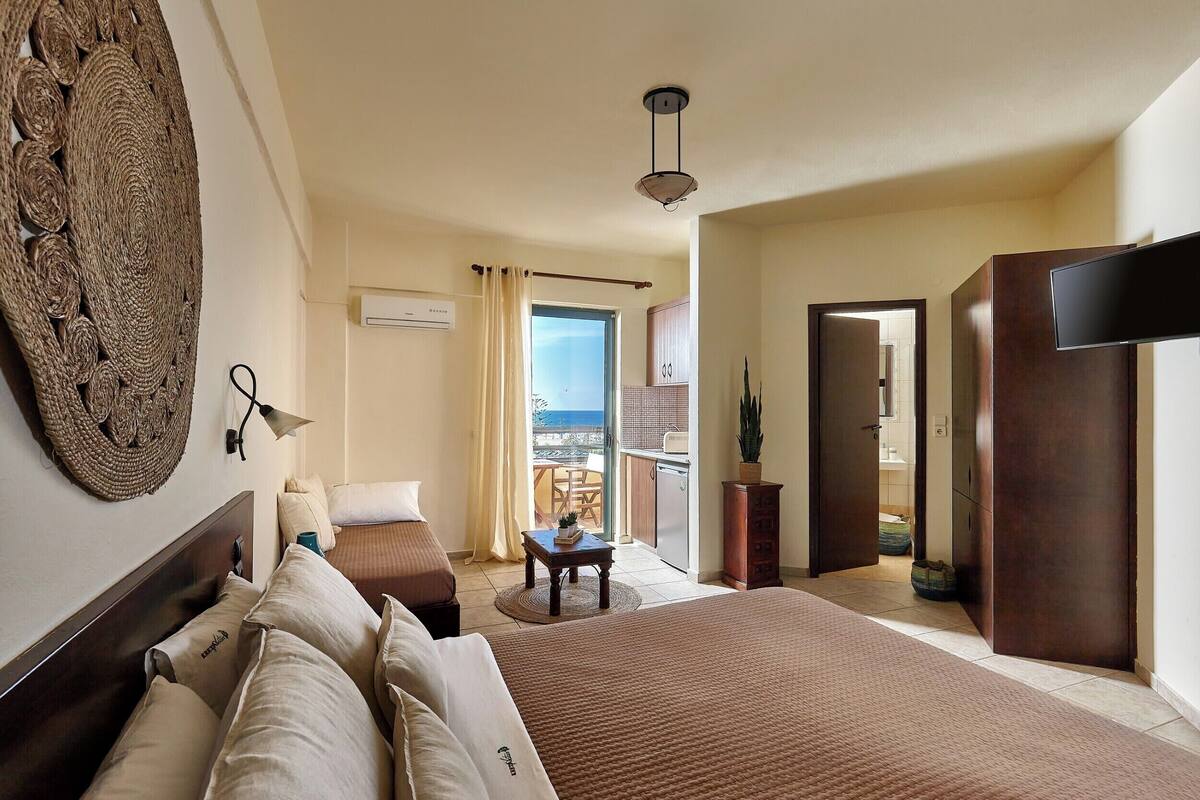 A hotel room with a large bed, a small table, a wall-mounted lamp, and a view of the balcony.