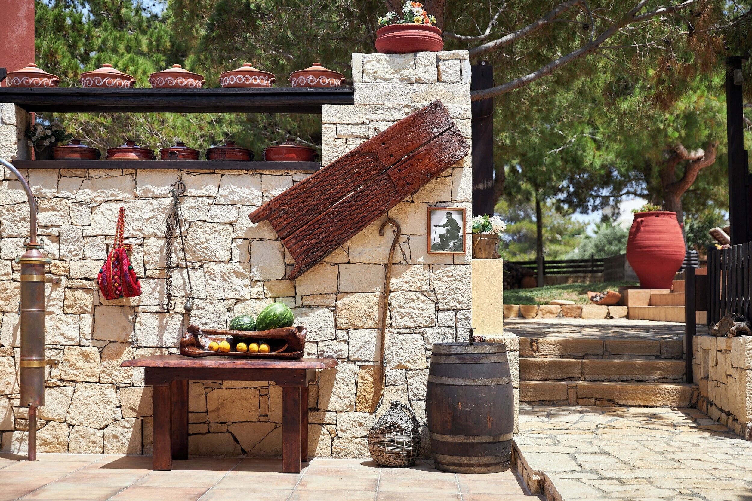 A stone wall with a rustic wooden table, potted plants, and a large barrel.