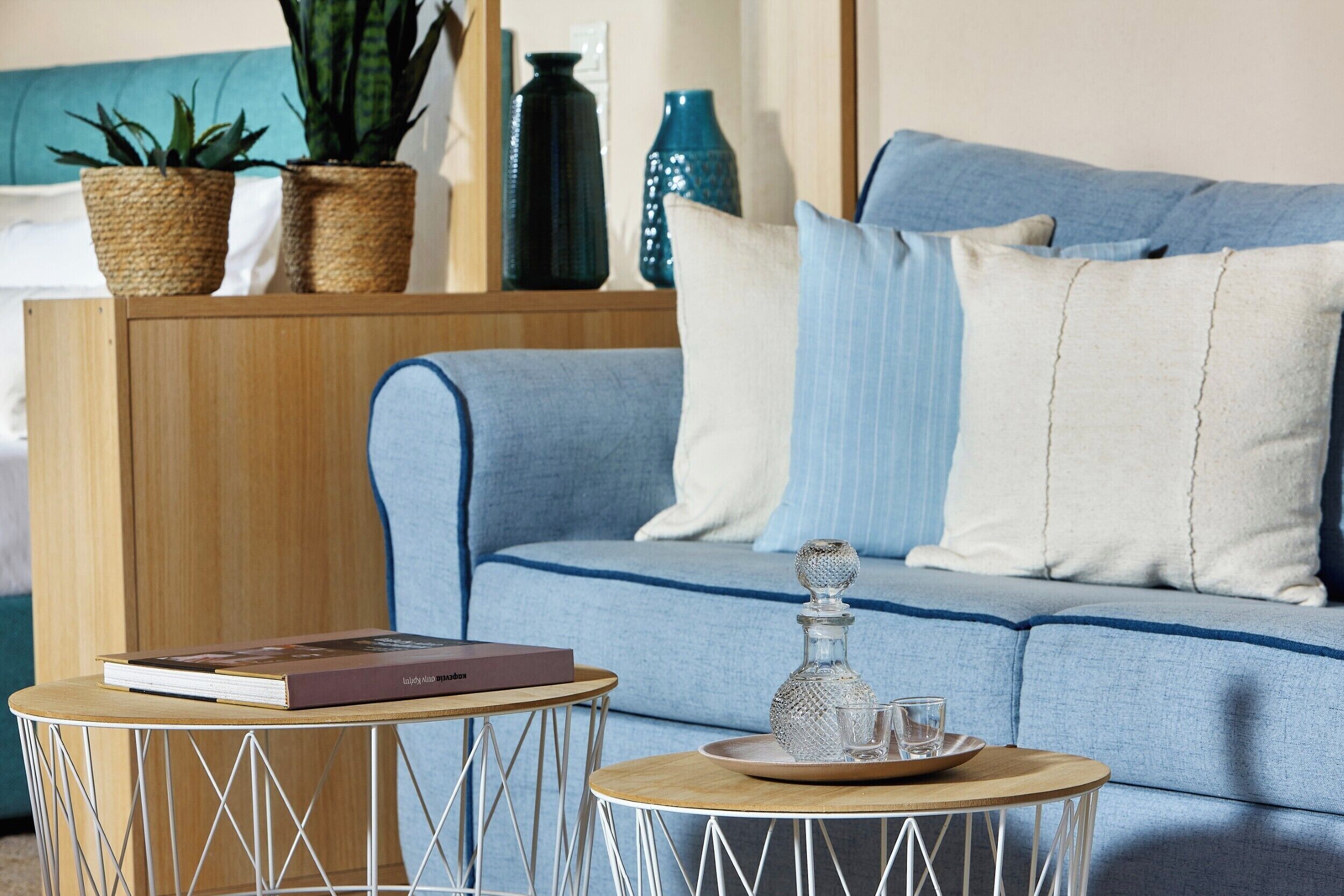 Un salón con un sofá azul, dos mesitas auxiliares, un libro, un decantador de vidrio y objetos decorativos.