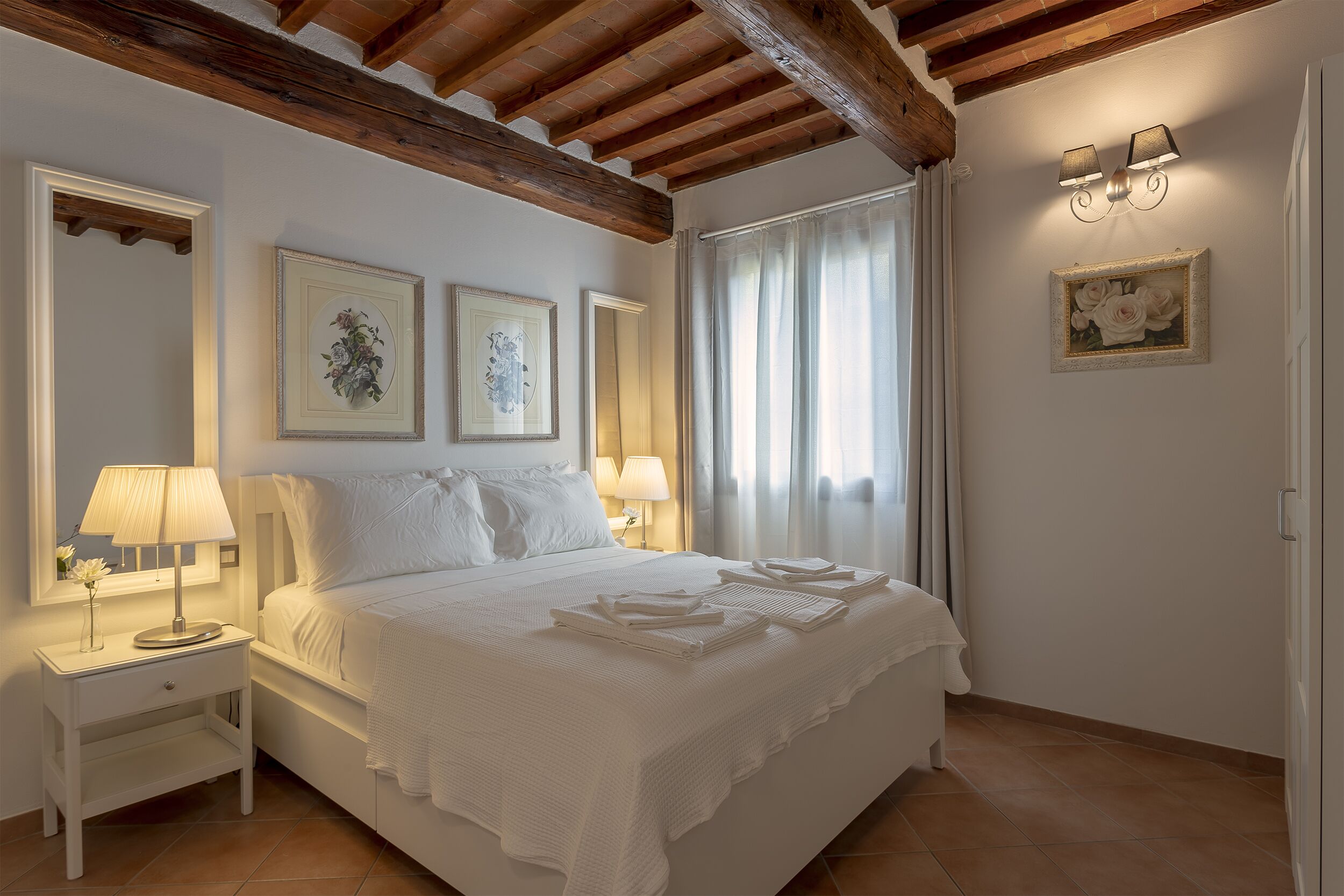 A bedroom with a bed, nightstands, wall-mounted lamps, and framed artwork.