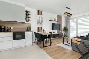 Eine moderne Küche mit eingebauten Geräten, ein Essbereich mit Tisch und Stühlen, ein Sofa und ein an der Wand befestigter Fernseher.