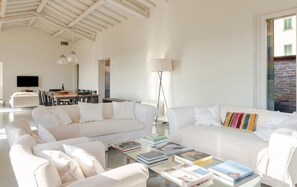 Ein modernes Wohnzimmer mit weißen Möbeln, einem Essbereich und einem großen Fenster.