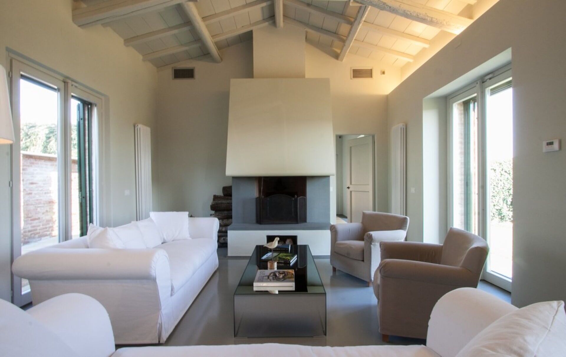 Een moderne woonkamer met een open haard, witte banken en een glazen salontafel.