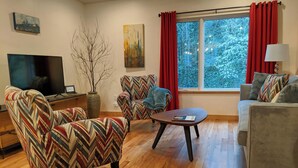 Een woonkamer met een televisie, twee fauteuils, een bank, een salontafel en een raam met gordijnen.