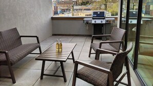 Een balkon met rieten meubilair, een barbecue en flessen op een tafel.