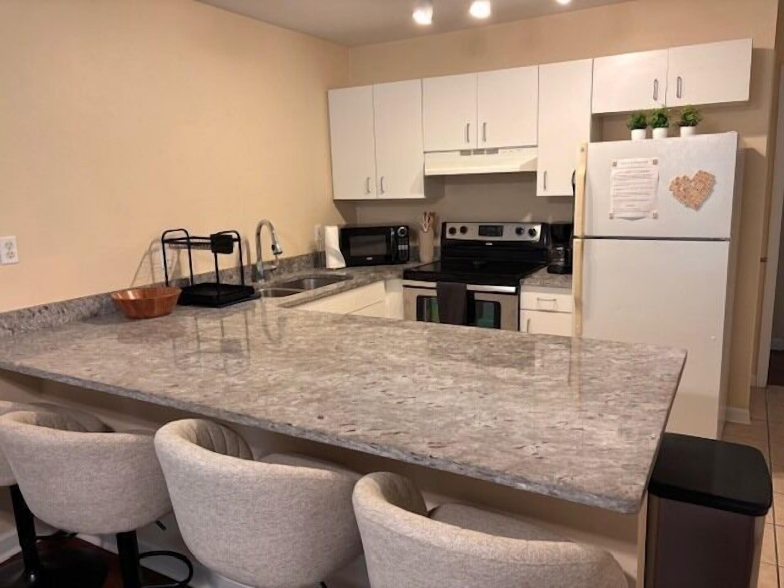 A kitchen with a granite countertop, white cabinets, a stove, microwave, and a refrigerator.