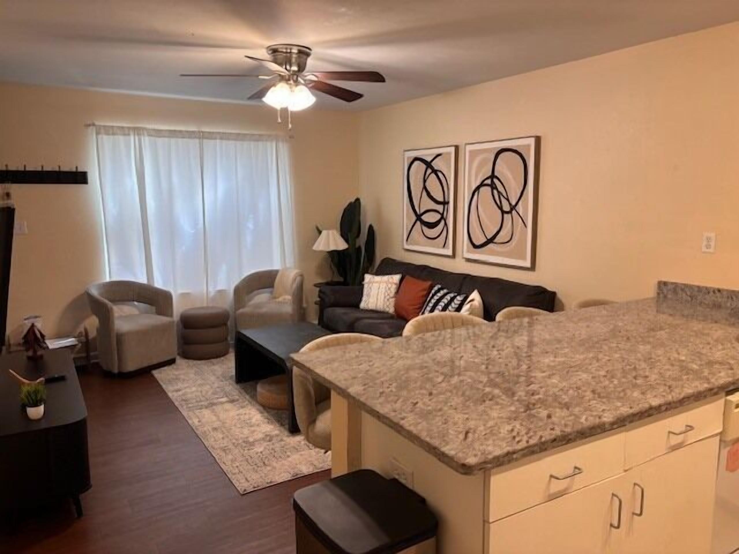 A modern living room with a kitchen island, a ceiling fan, and abstract wall art.