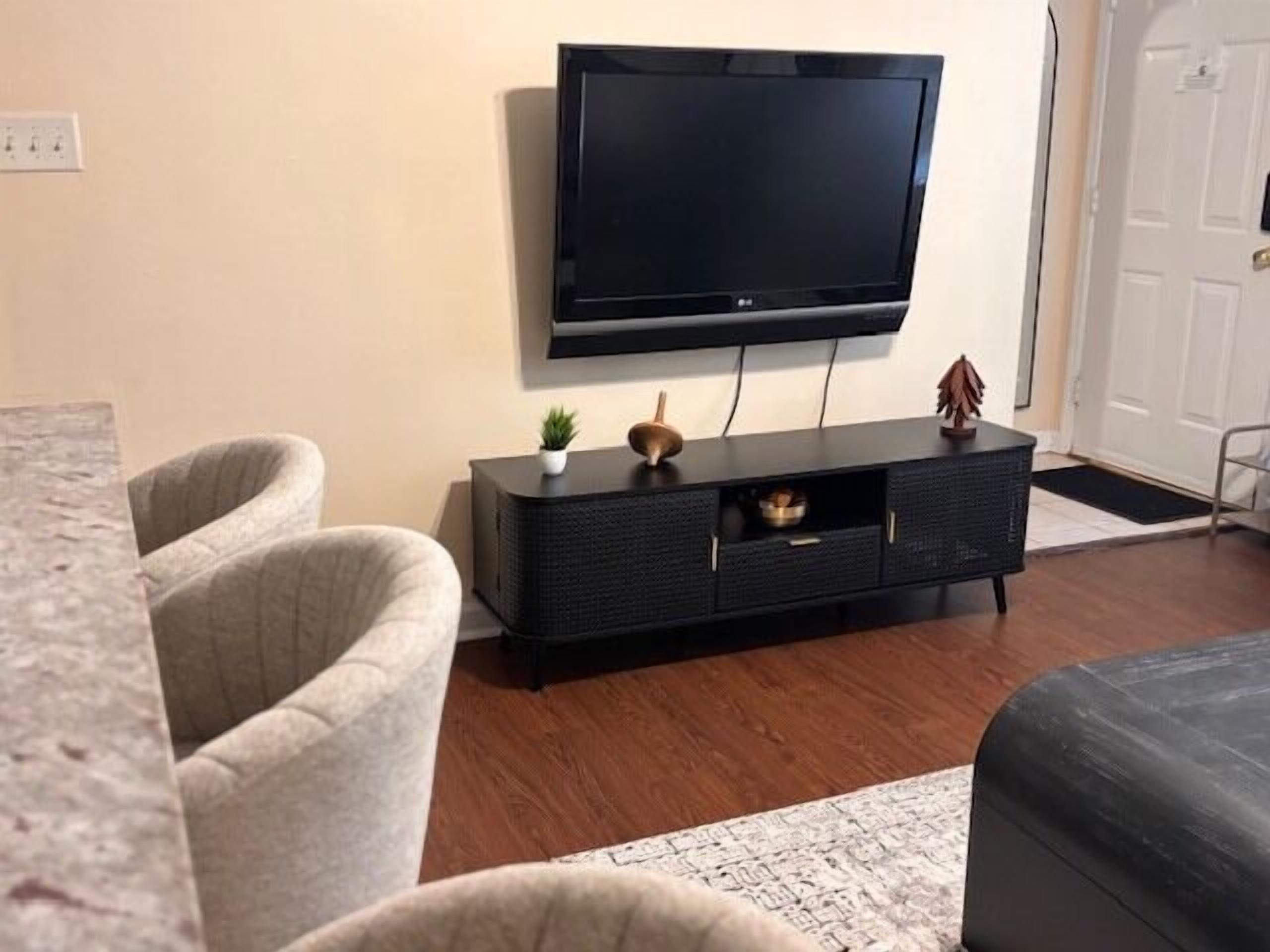 A living room with a flat-screen TV mounted on the wall, a dark-colored entertainment unit, and two grey sofas.