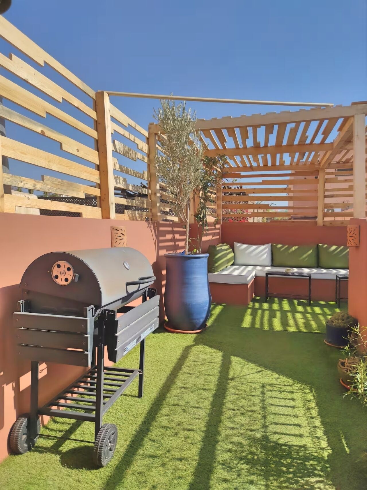 A patio with a grill, a large planter, and a seating area with cushions.