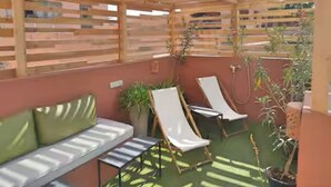 Een terras buiten met een houten pergola, een groene bank, twee loungesteunen en potplanten.