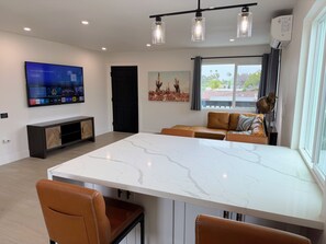 Ein modernes Wohnzimmer mit großem Fernseher, einem Marmorestisch, Ledersesseln, einer schwarzen Tür und einem Fenster mit Blick.