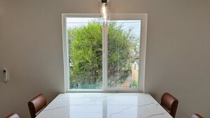 A dining area with a marble table, leather chairs, a hanging light fixture, and a window with a view of greenery. - Brand New next to Balboa Park, near Little Italy (San Diego)
