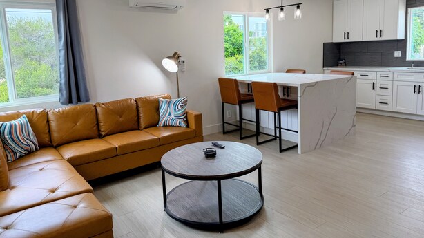 A modern living space with a leather sofa, a round table, a kitchen area with white cabinets, and a large window. - Brand New next to Balboa Park, near Little Italy (San Diego)