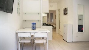 Una cocina moderna con muebles blancos, un rincón comedor con dos sillas y una pequeña isla.