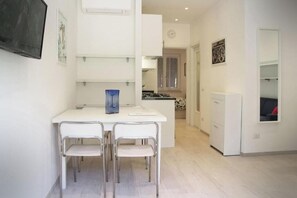 A modern kitchen with white cabinetry, a dining area with two chairs, and a small island. - Apartment Fezzano di Portovenere L'ONDA 1 (Fezzano di Portovenere)