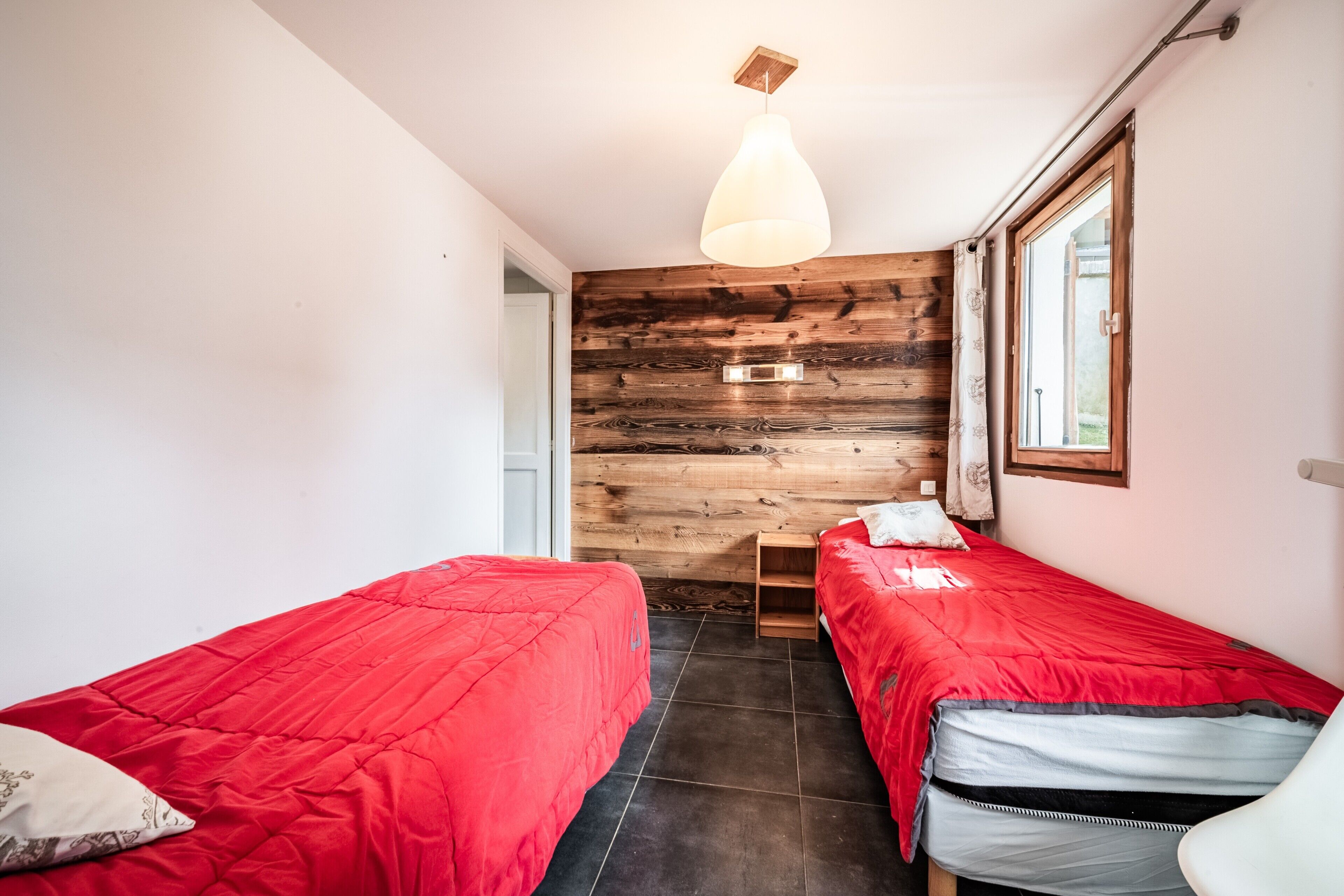 Een kamer met twee bedden, een houten wand, een raam en een hanglamp.