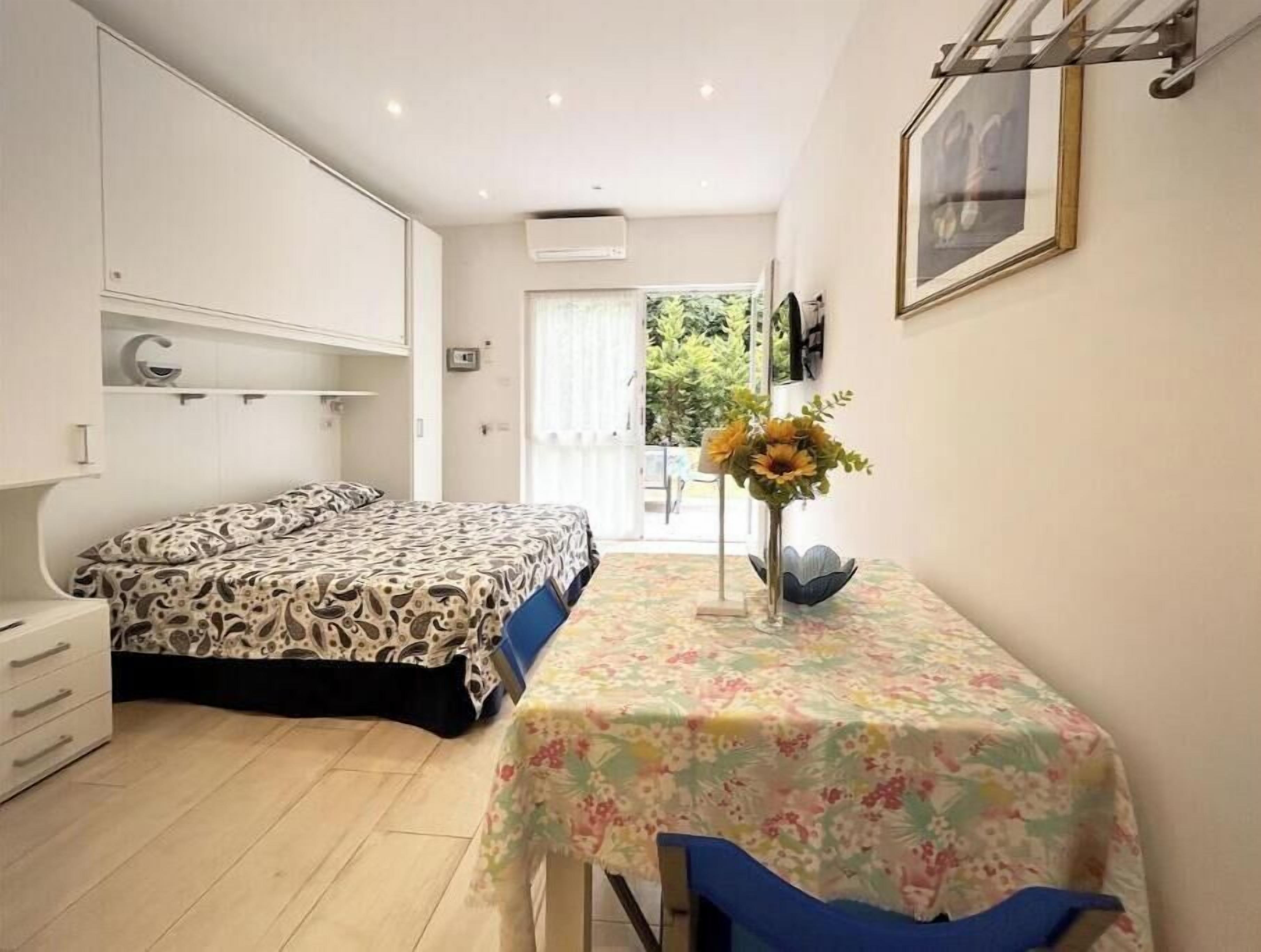 A bedroom with a bed, a desk with a chair, a window, and a door leading outside.