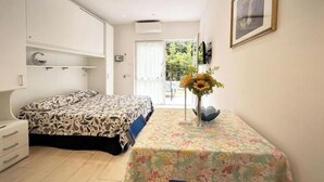 Une chambre à coucher comprenant un lit, un bureau avec une chaise, une fenêtre et une porte donnant sur l’extérieur.