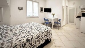 Ein Schlafzimmer mit einem Bett, einem kleinen Tisch mit Stühlen, einem Fernseher und einer Küchenzeile.