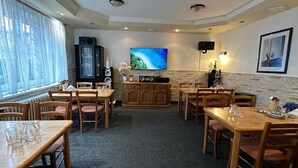 A dining area with multiple tables and chairs, a television mounted on the wall, and a cabinet with speakers. - Pezion and apartman near Karlovy Vary (Chodov)