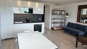 A modern kitchen with white cabinets, a dining table, and a sofa in a living area. - Mer et soleil appartements (Cogolin)
