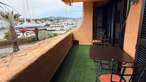 A balcony with a view of a marina, a table, chairs, and a small patch of artificial grass. - Mer et soleil appartements (Cogolin)