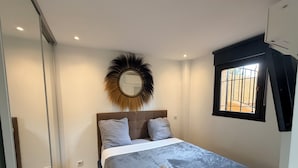 A bedroom with a bed, a round mirror, a window, and a ceiling fan. - Mer et soleil appartements (Cogolin)