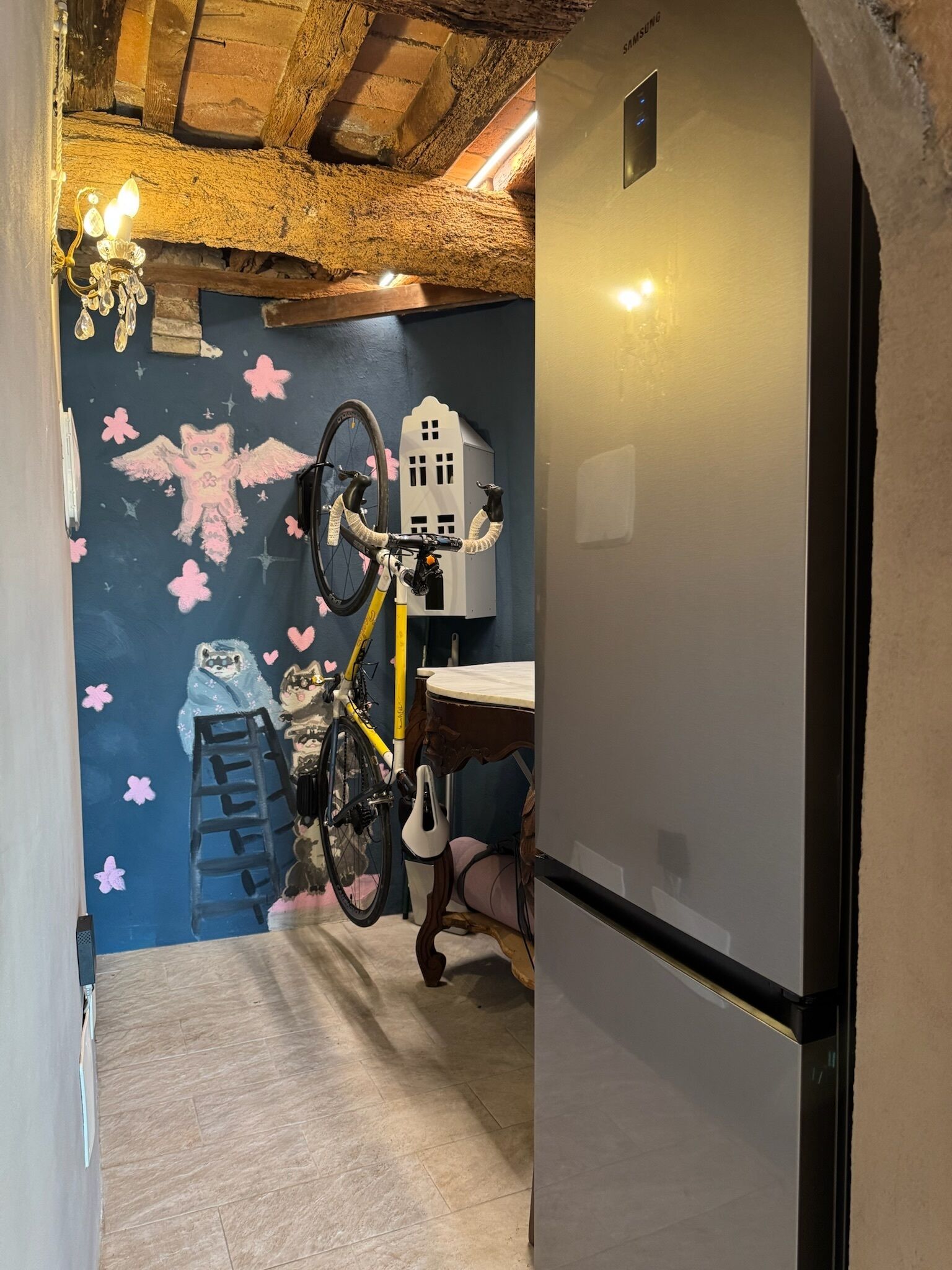 Une cuisine équipée d’un réfrigérateur, d’un support mural pour vélos et d’une fresque représentant une échelle et des personnages.