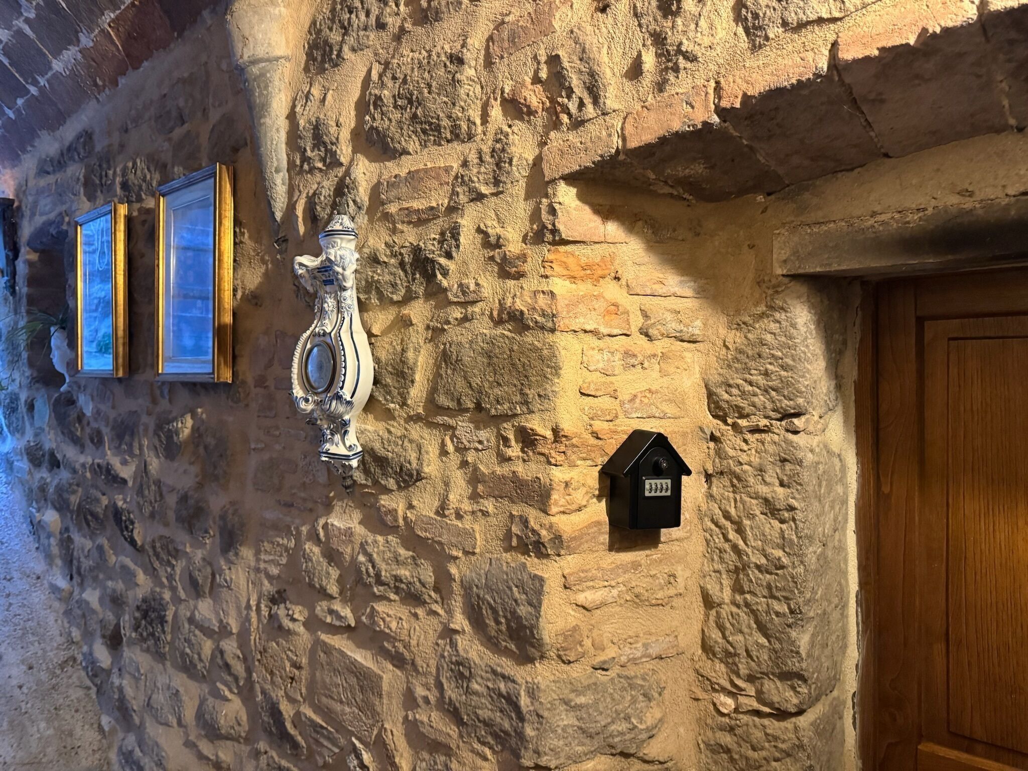 Un mur de pierres avec une porte en bois, une boîte aux lettres noire et deux tableaux encadrés.