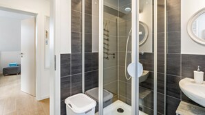 A modern bathroom with a glass-enclosed shower, dark tiled walls, a white sink, and a visible toilet. - Modern Apartment – Quiet & Prime Location in Neheim (Arnsberg)