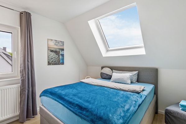 A bedroom with a bed, a window, a painting, and a radiator.