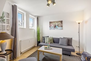 A modern living room with a sofa, a coffee table, a floor lamp, a radiator, and a window with curtains.